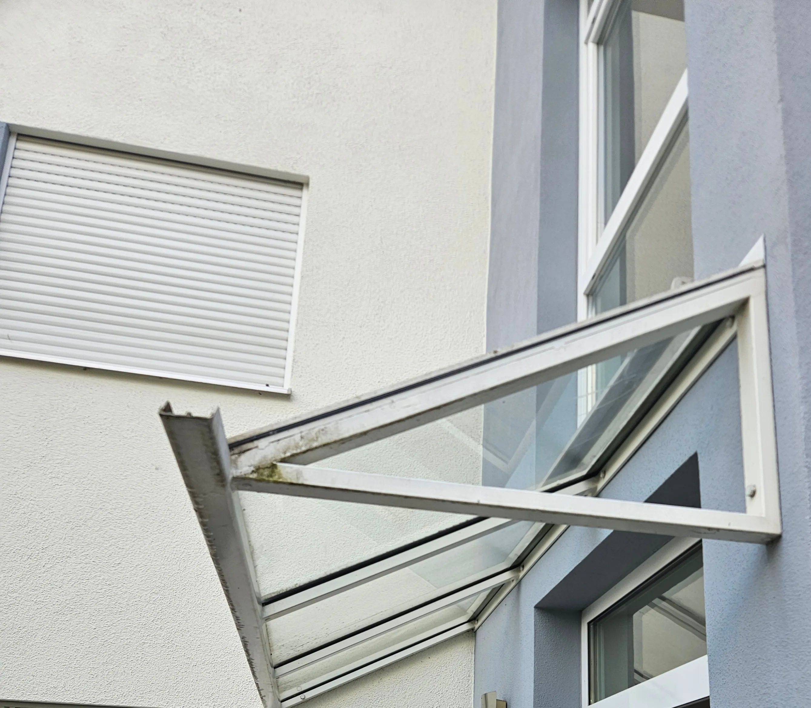 Glasvordach mit sichtbaren Ablagerungen am Aluminiumrahmen