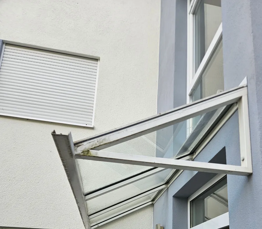 Glasvordach mit sichtbaren Ablagerungen am Aluminiumrahmen